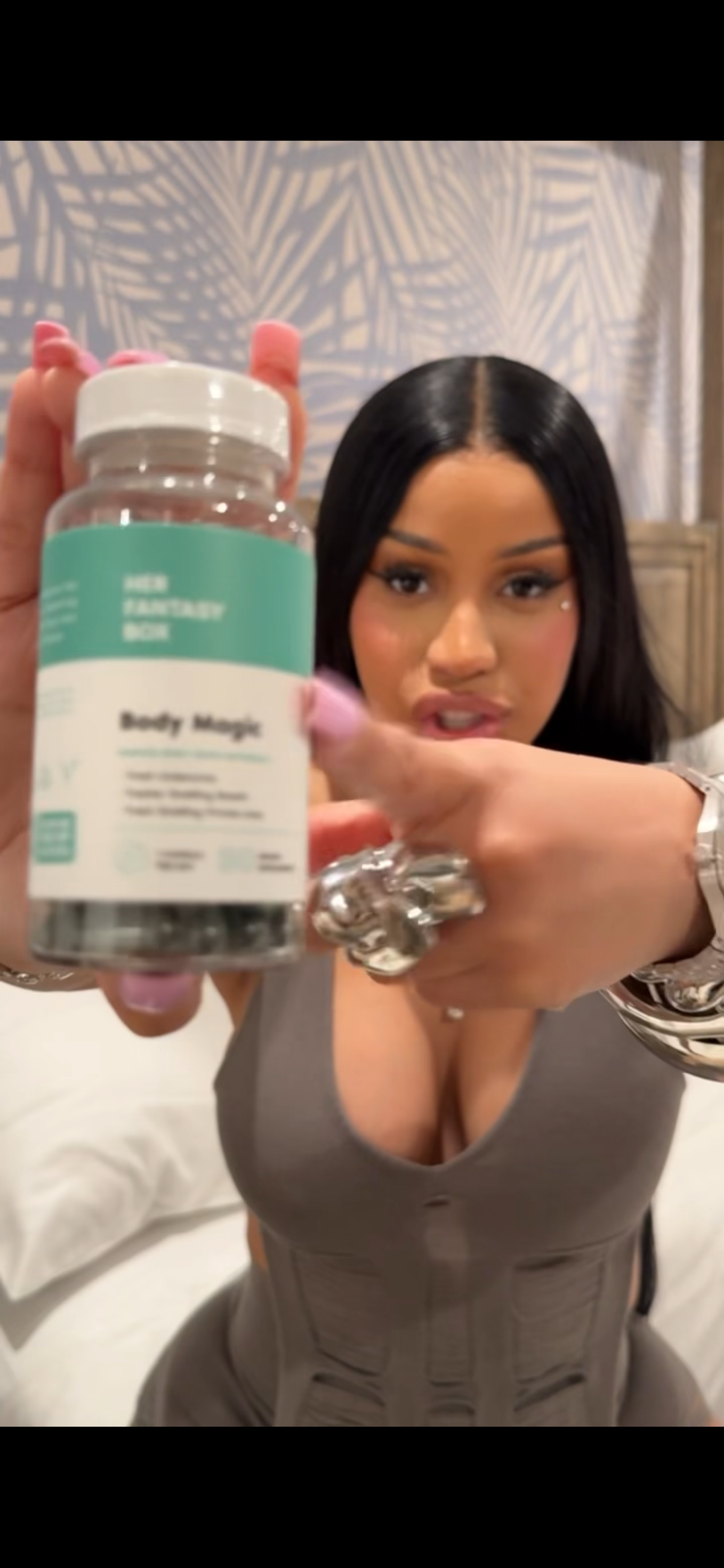 Woman holding Her Fantasy Box Body Magic dietary supplement bottle toward camera.