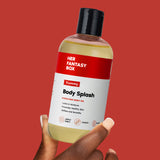 Hand holding Her Fantasy Box Yummy Body Splash hydrating body oil bottle against bold red background
