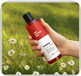 A hand holding Her Fantasy Box Yummy full body cleansing gel held outdoors over a daisy field