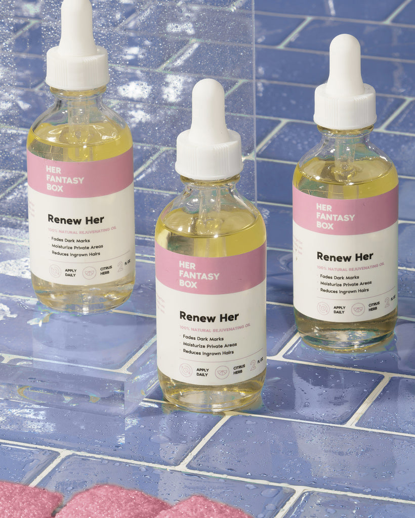 Three bottles of Her Fantasy Box Renew Her 100% natural rejuvenating oil displayed on blue tile for fading dark marks and ingrown hairs