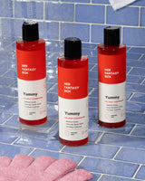 Three bottles of 'Her Fantasy Box Yummy' body wash on a blue tiled bathroom floor