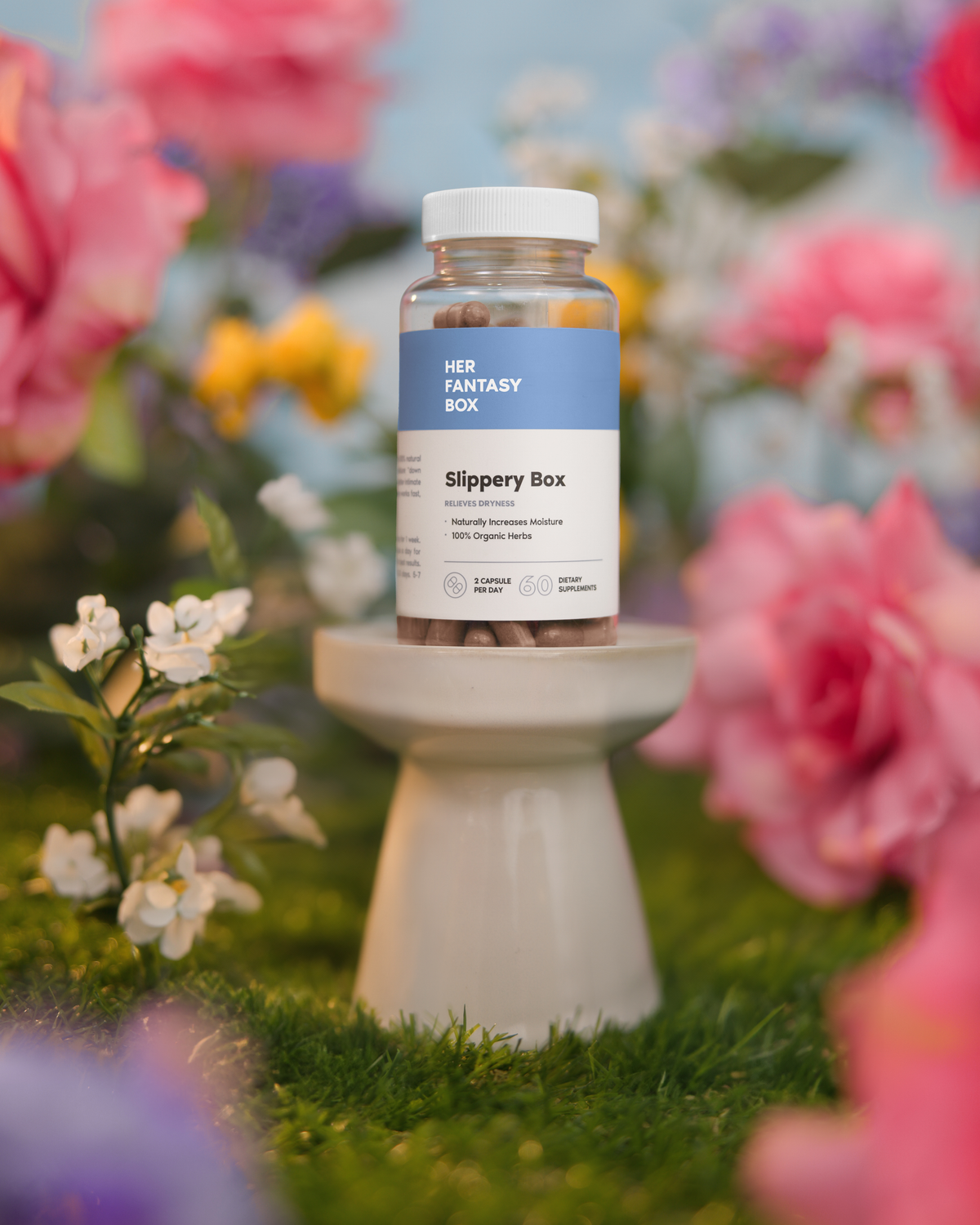 A bottle of Slippery Box capsules placed on a stand with a floral background.