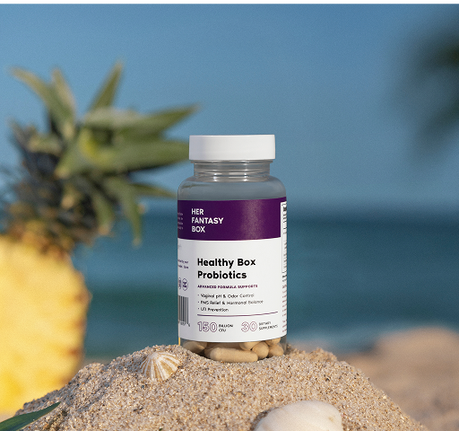 Her Fantasy Box Healthy Box Probiotics bottle on a sandy surface with a blurred beach background