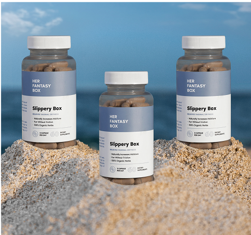 Three bottles of 'Her Fantasy Box' on a sandy surface with a blue sky background