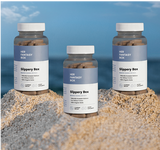 Three bottles of 'Her Fantasy Box' on a sandy surface with a blue sky background