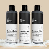 Three bottles of Her Fantasy Box Charcoal Detox Steamy Eucalyptus exfoliating body wash 16 fl oz displayed together on neutral background with lather