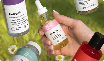 Hand holding a bottle of skincare product with other bottles in the background on a grassy field.